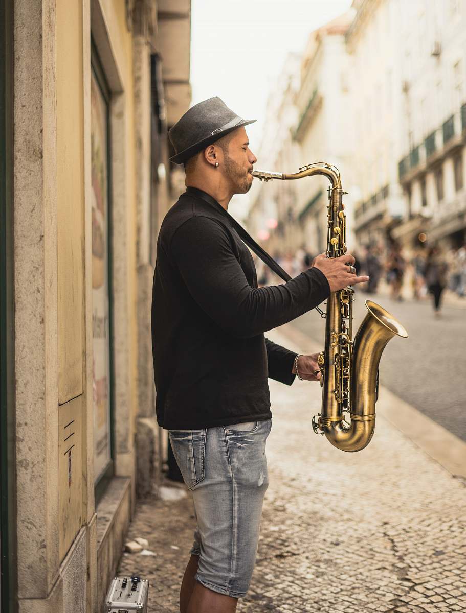 musical instrument man playing copper-colored saxophone on street during daytime saxophone